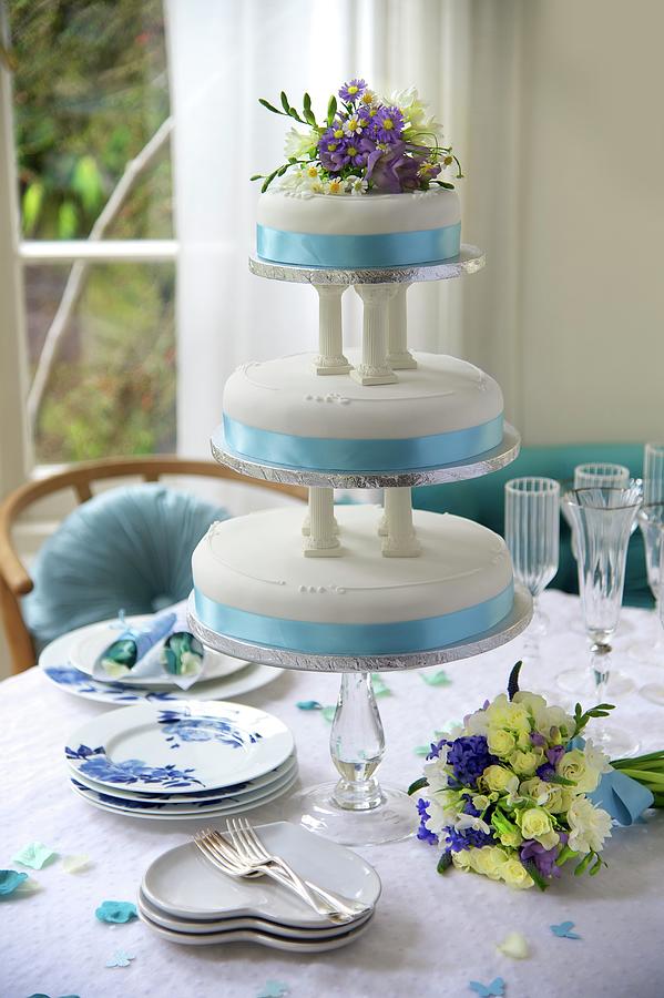 A Three-tier, Blue And White Wedding Cake Decorated With Flowers On A Festively Laid Table Photograph by Winfried Heinze
