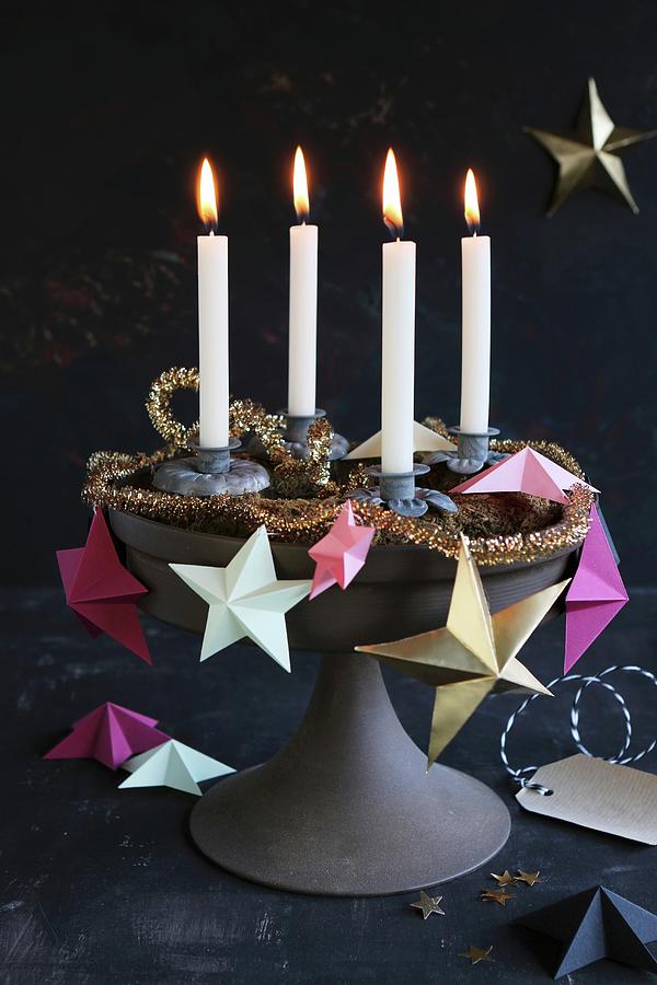 A Unique Advent Wreath On A Cake Stand Decorated With Paper Stars, A Golden Garland And Four Burning Candles Photograph by Regina Hippel