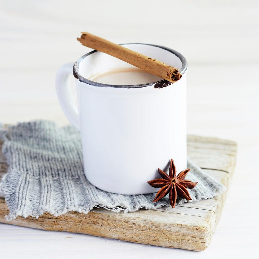 A White Enamel Mug Of Tea, With A Cinnamon Stick Across The Top And A Star Anise Resting Against The Mug; The Ensemble Is On A Piece Of Grey Knitting On A Weathered Board Photograph by Sonia Chatelain