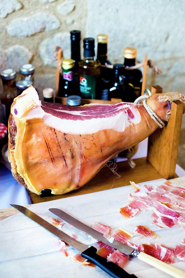 A Whole Air Dried Ham On A Wooden Stand With Knives, Bottles And A Chopping Board Photograph by Jamie Watson