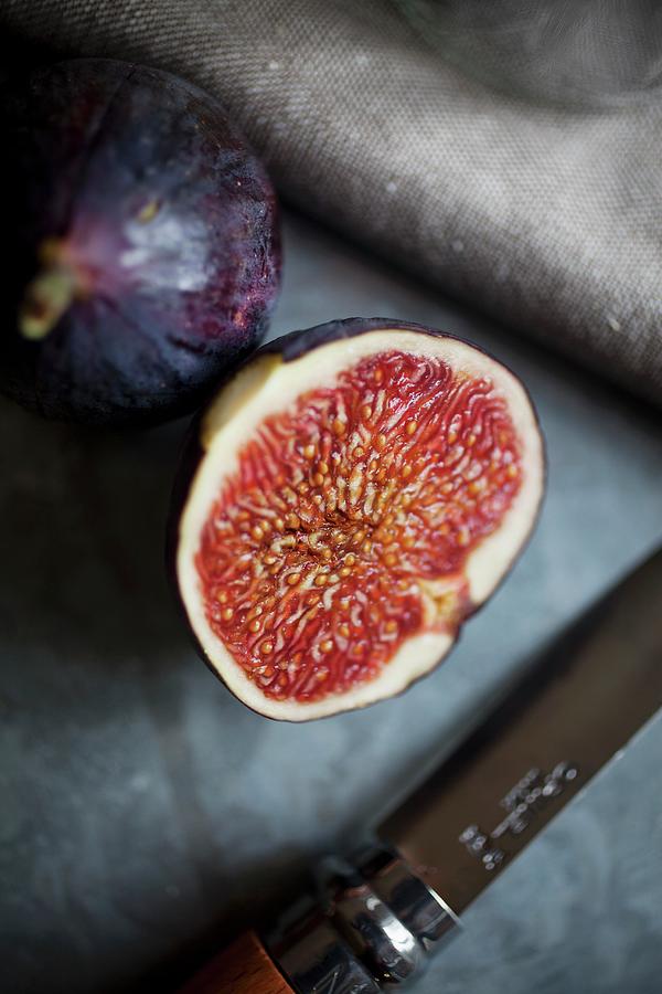 A Whole Fig And A Halved Fig On A Galvanised Surface With A Linen Cloth And A Knife Photograph by Victoria Harley