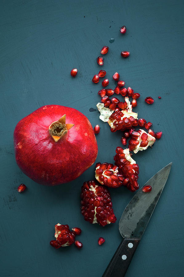 A Whole Pomegranate And Pomegranate Pieces With A Knife On A Blue Background Photograph by Achim Sass