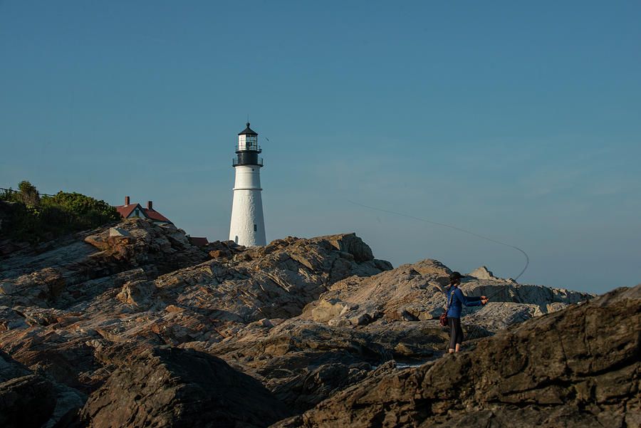 Portland Photograph - A Woman Fly Fishing Near A Lighthouse On The Coast Of Maine by Cavan Images
