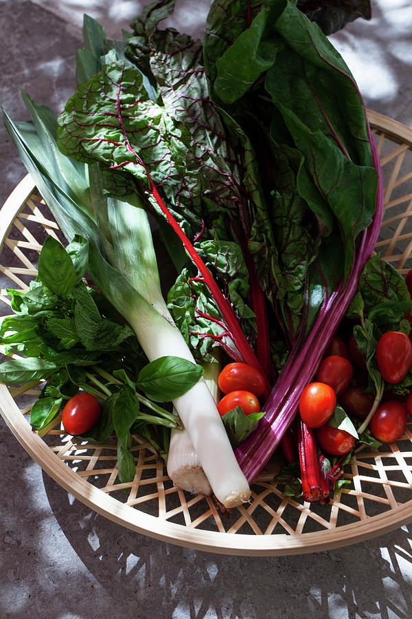 A Wooden Basket On An Outdoor Stone Surface, Filled With Rainbow Swiss Chard, Tomatoes, Leeks, Mint And Basil Photograph by Ryla Campbell