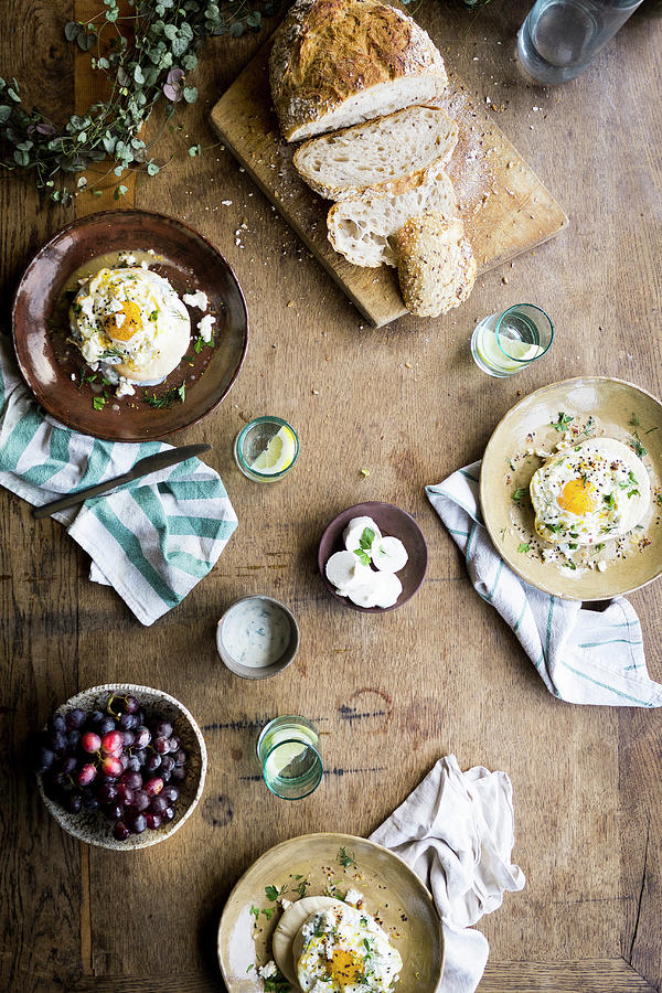 A Wooden Table With Frioed Eggs, Sourdough Bread, Grapes, Water In Glasses And Goat Cheese Photograph by Lucie Beck
