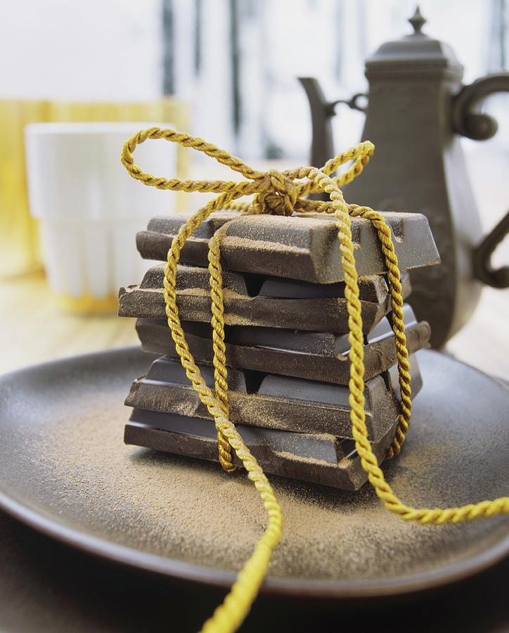 A Yellow Cord Tied Around Pieces Of Chocolate, On A Ceramic Dish In Front Of A Vintage Coffee Pot Photograph by Matteo Manduzio
