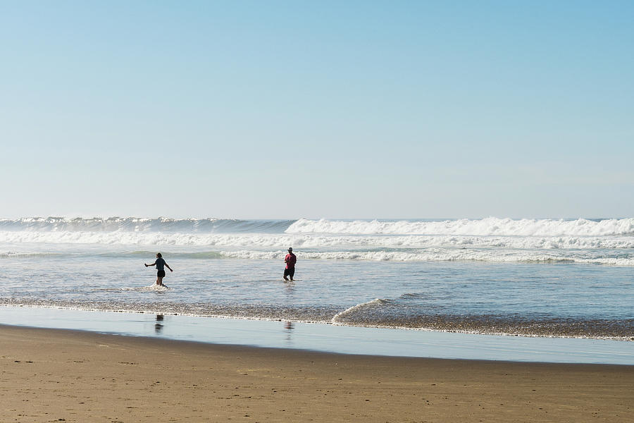A Young Couple Play To Escape From The Wave That Just Caught Thecannon Beach, Oregon, Usa - October Photograph