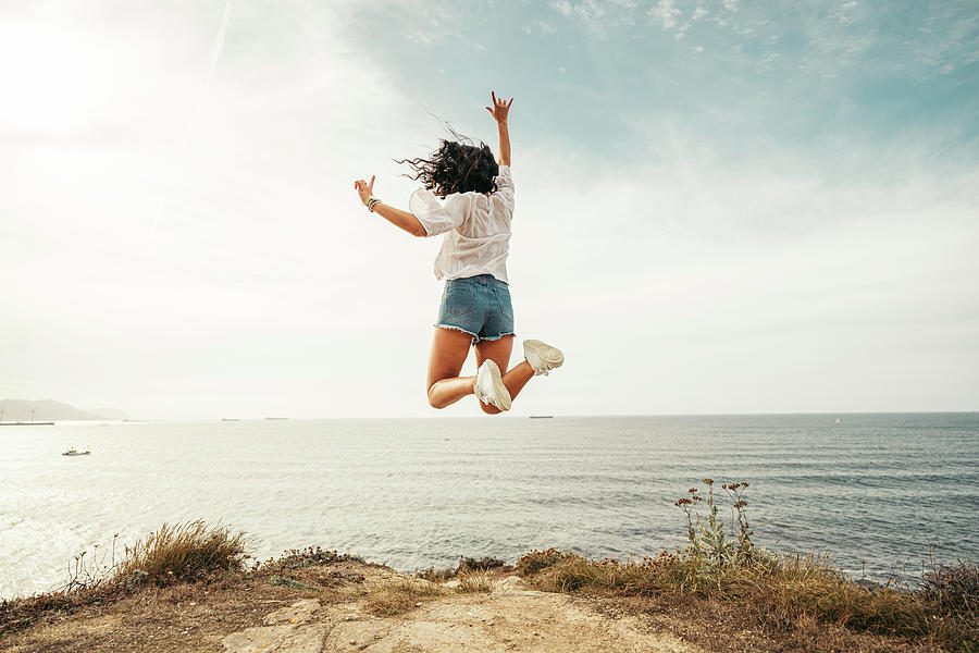 A Young Woman Jumping On The Edge Of A Cliff In Front Of The Sea Photograph by Cavan Images - Pixels