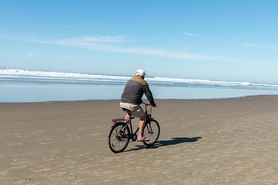 An Adult Man In A White Cap And Flip-flops Rides His Bike Througcannon Beach, Oregon, Usa - October Photograph