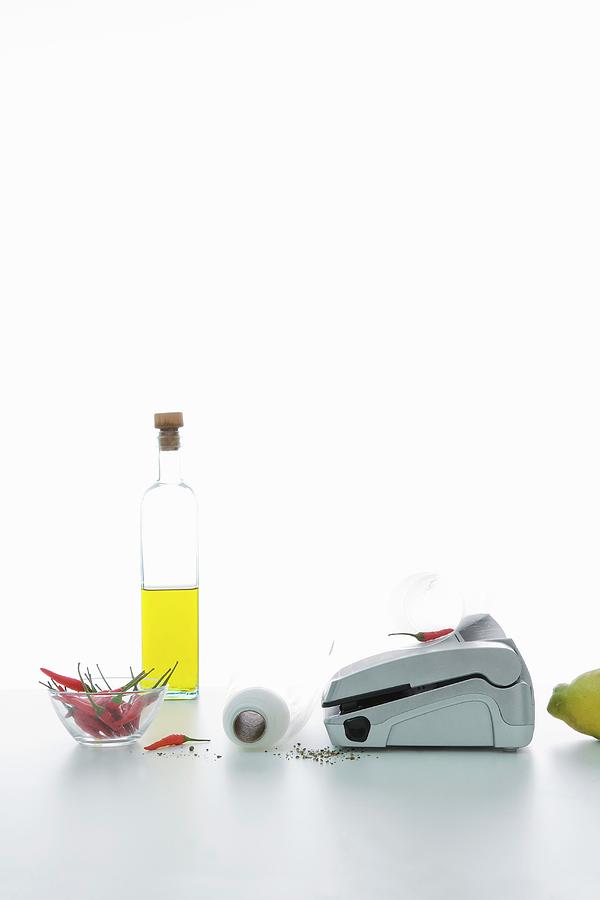 An Arrangement Featuring A Vacuum Packaging Machine, A Bottle Of Oil And Chilli Peppers Photograph by Michael Wissing