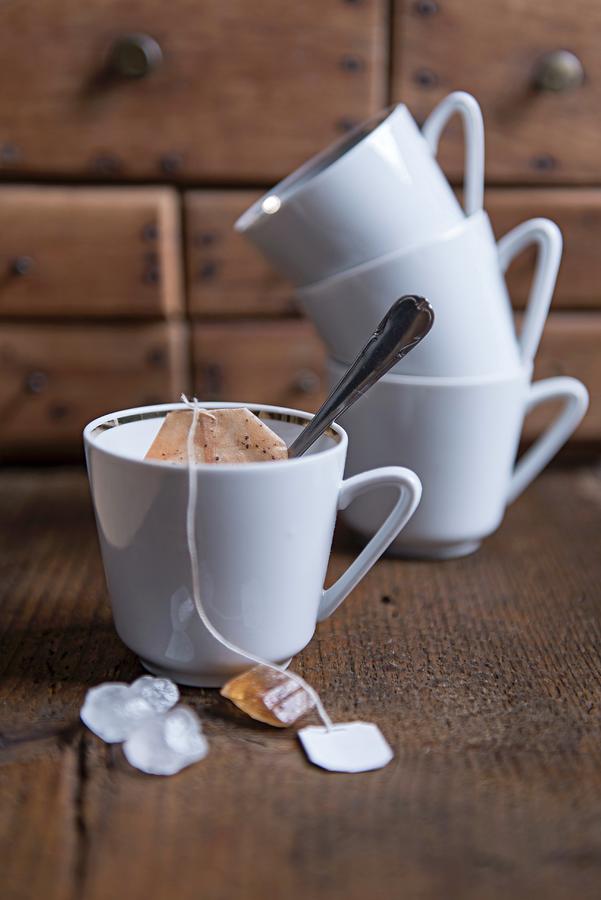An Arrangement Of White Tea Cups, A Used Tea Bag And Rock Sugar Photograph by Angelika Grossmann