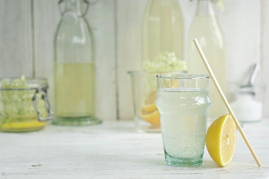 An Elderflower Drink In A Glass With A Straw And Homemade Elderflower Cordial In Bottles Photograph by Achim Sass