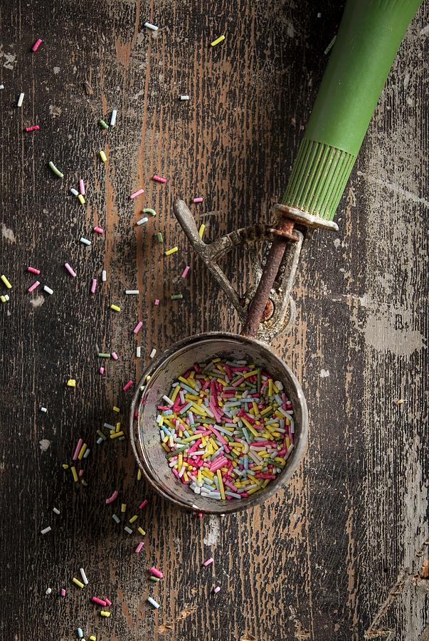 An Old Ice Cream Scoop With A Green Handle Filled With Colourful Sugar Sprinkles On A Wooden Surface Photograph by Stacy Grant