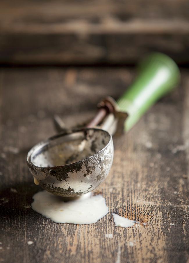 An Old Ice Cream Scoop With A Green Handle In A Pool Of Melted Vanilla Ice Cream On A Wooden Surface Photograph by Stacy Grant