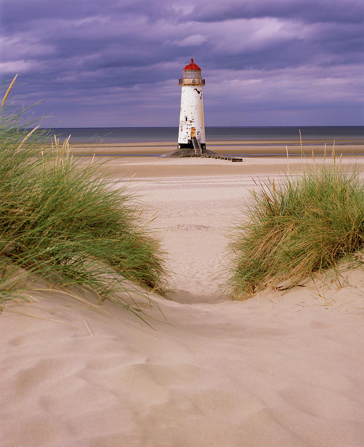 An Old White Lighthouse With A Red Roof On A Sandy Beach With Gr