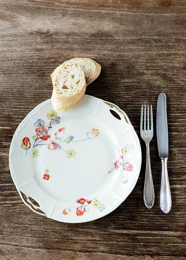 An Old White Porcelain Plate Decorated With Flowers With Silver Cutlery And Two Slices Of Baguette On The Wooden Table Photograph by Julia Hildebrand