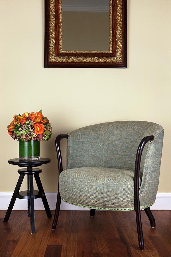An Upholstered Armchair With A Mottled Grey Cover And A Black, Height-adjustable Side Table In Front Of A Pastel-coloured Wall Photograph by Amy Kalyn Sims