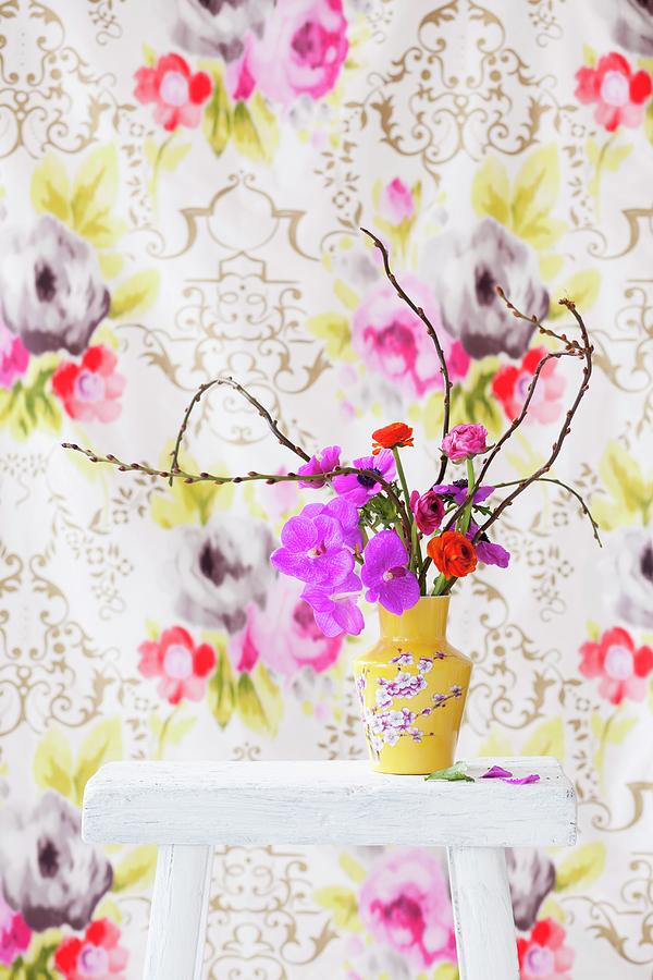Anemones, Ranunculus And Orchids In Yellow, Floral Vase Against Floral Wallpaper Photograph by Peter Kooijman