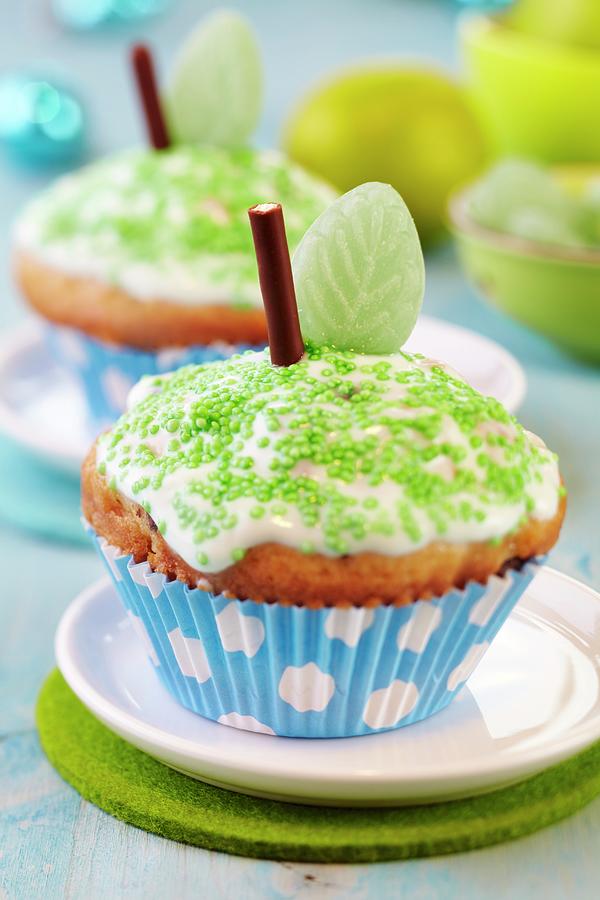 Apple Muffins Decorated As Apples With Icing, Green Sprinkles, Chocolate Sticks And Leaf-shaped Sweets Photograph by Franziska Taube