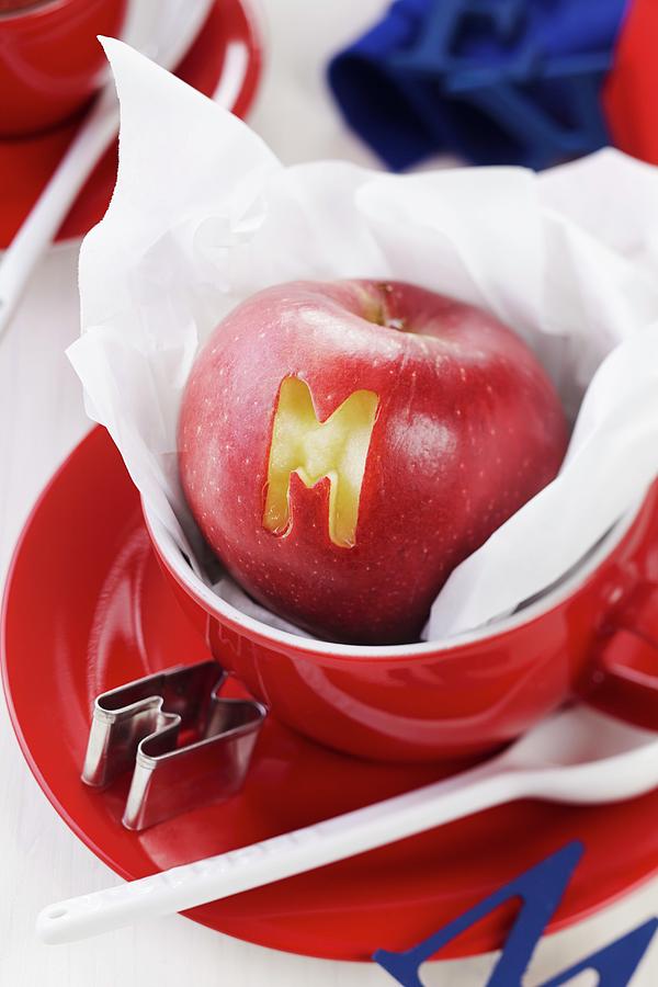 Apple With Letter Cut-out In Red Cup Photograph by Franziska Taube
