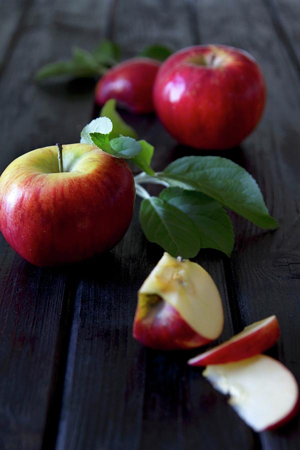 Apples With Leaves, Whole And Chopped, On A Wooden Surface Photograph by Catja Vedder