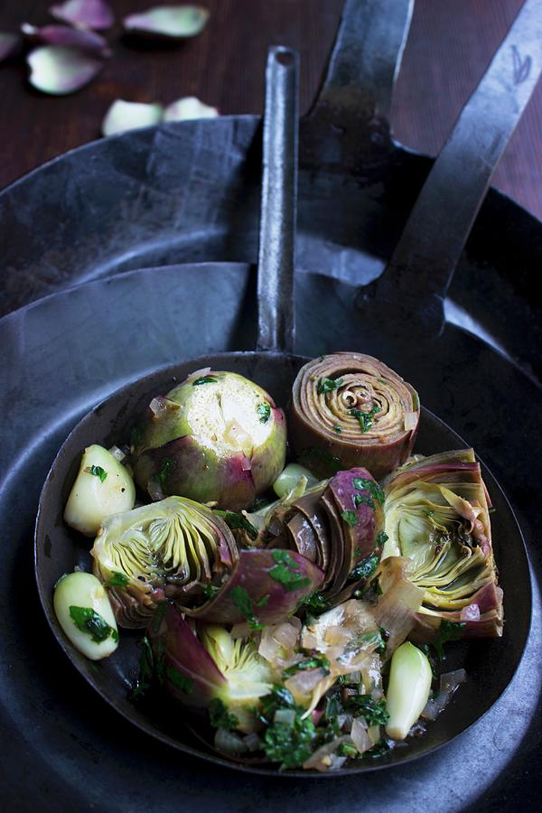 Artichokes With Herbs And Garlic In A Hand-forged Iron Pan Photograph by Charlotte Von Elm