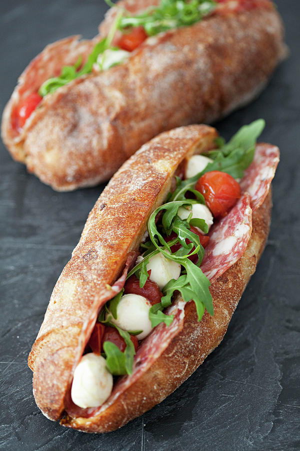 Artisan Baguettes On A Slate Filled With Salami, Tomatoes, Mozzarella Balls And Rocket Photograph by Steven Joyce