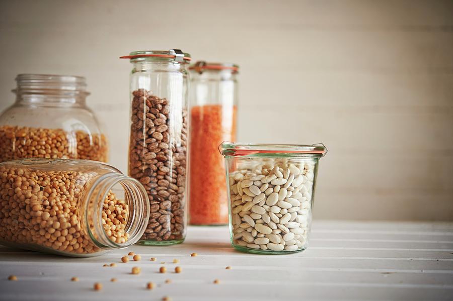 Assorted Jars Of Beans And Grains On Wooden Surface Including Corn, Lentils, Pinto Beans, Canellini Beans, And Peas Photograph by Greg Rannells
