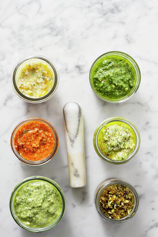 Assorted Jars Of Pesto On A Marble Surface With A Pestle Photograph by Marie Sjoberg