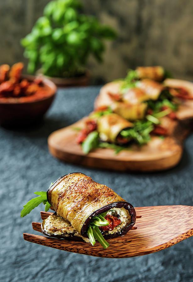 Aubergine Rolls Filled With Sheeps Cheese, Rocket And Dried Tomatoes On A Wooden Fork And A Wooden Board Photograph by Julian Winkhaus