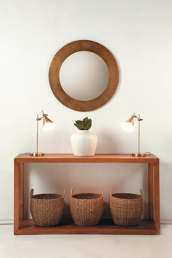 Bamboo Baskets, Table Lamps And Vase On Wooden Console Table Below Round Mirror On Wall Photograph by Great Stock!