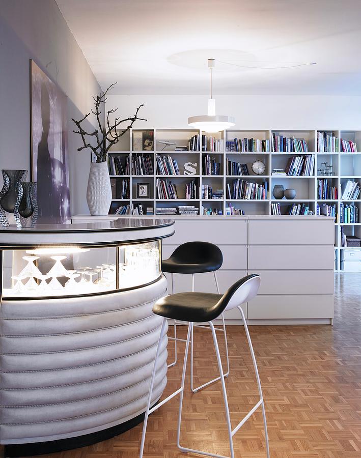 Bar Stool At Semicircular Bar With Illuminated Glass Top Next To Half-height, White Chest Of Drawers Used As Partition In Front Of Bookcase Photograph by Stefan Thurmann