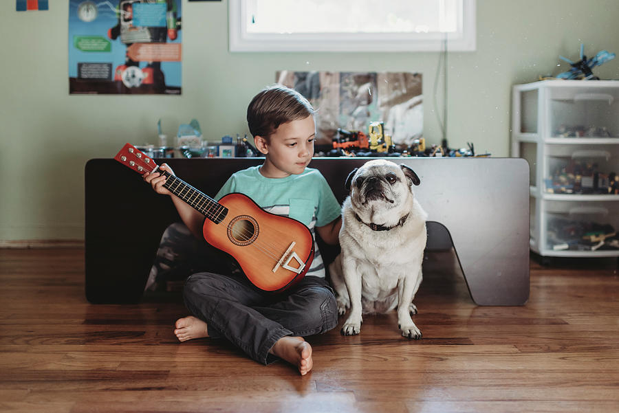 Toy Photograph - Barefoot Boy Holding Guitar Sitting Next To Pet Pug On Hardwood Floor by Cavan Images