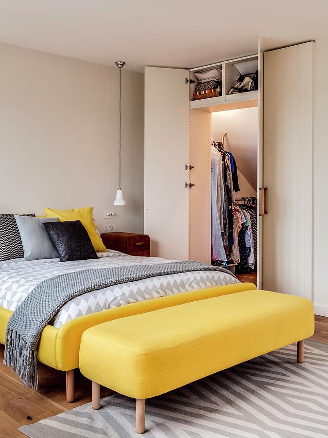 Bed With Yellow Upholstered Frame Next To Open Fitted Wardrobe Under Sloping Ceiling Photograph