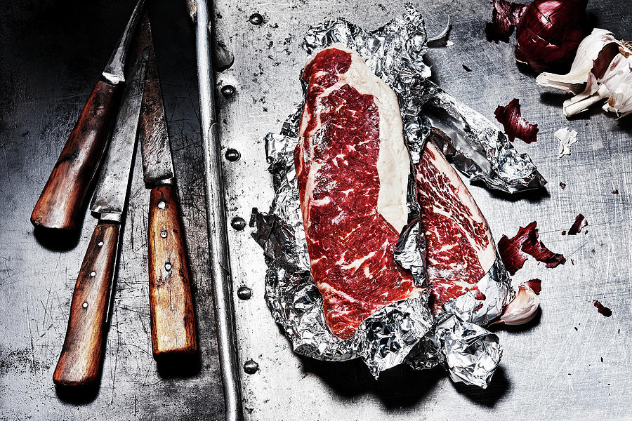 Beef Steaks In Aluminium Foil Next To Old Knives Photograph by Manfred Rave