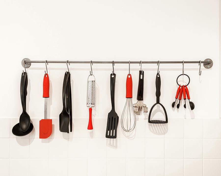 Black And Red Kitchen Utensils Hung From Hooks On Bar Photograph by Stuart Cox
