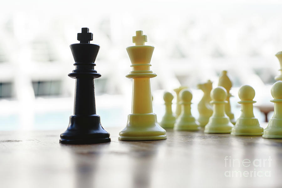 Black and white chess kings faced between defocused pieces on wooden board. Photograph by Joaquin Corbalan