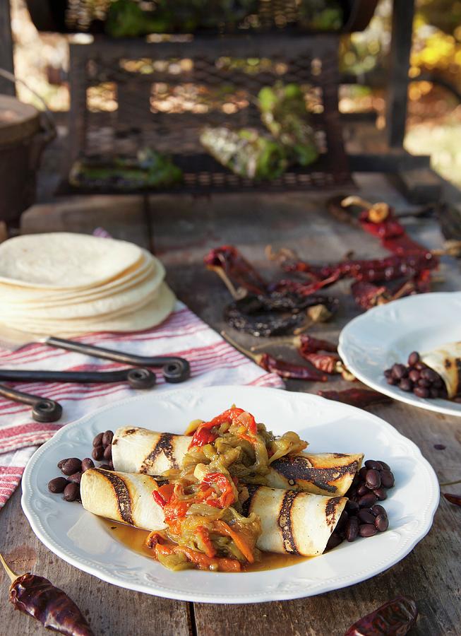 Black Bean Burritos And Roasted Chilli Peppers On A Wooden Table Outdoors Photograph by Katharine Pollak
