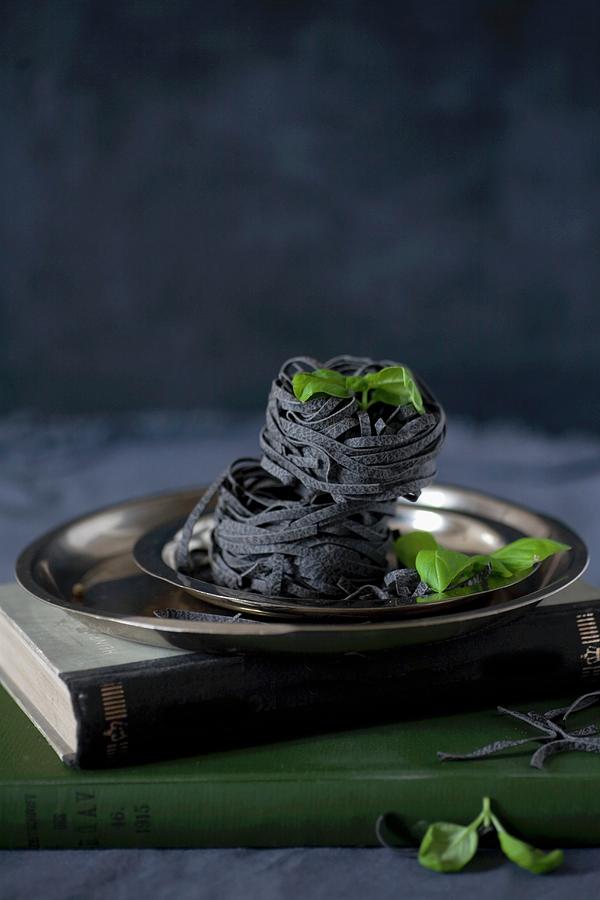 Black Ribbon Noodles And Basil Leaves On A Metal Plate Photograph by Alicja Koll