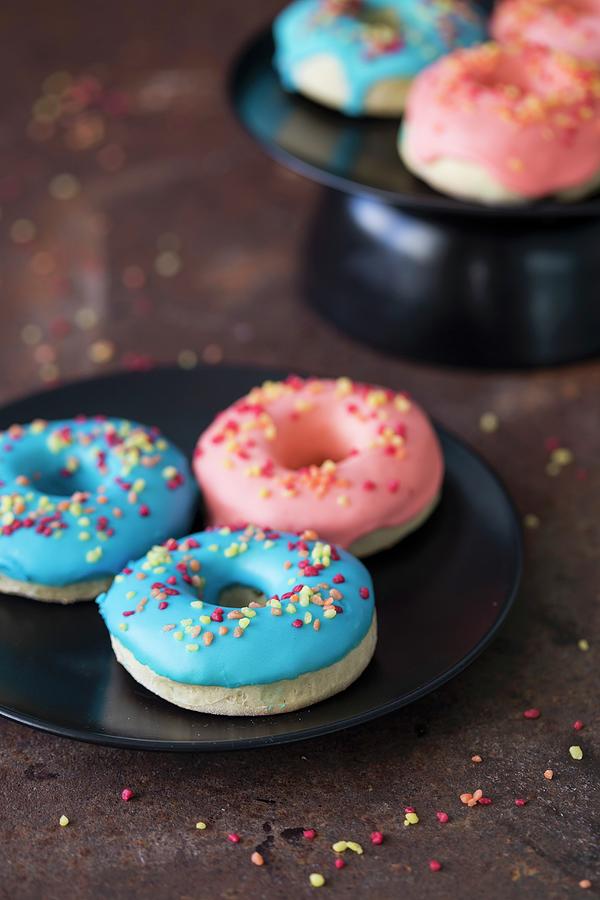 Blue And Pink Glazed Doughnuts With Sugar Sprinkles On A Plate Photograph by Malgorzata Laniak