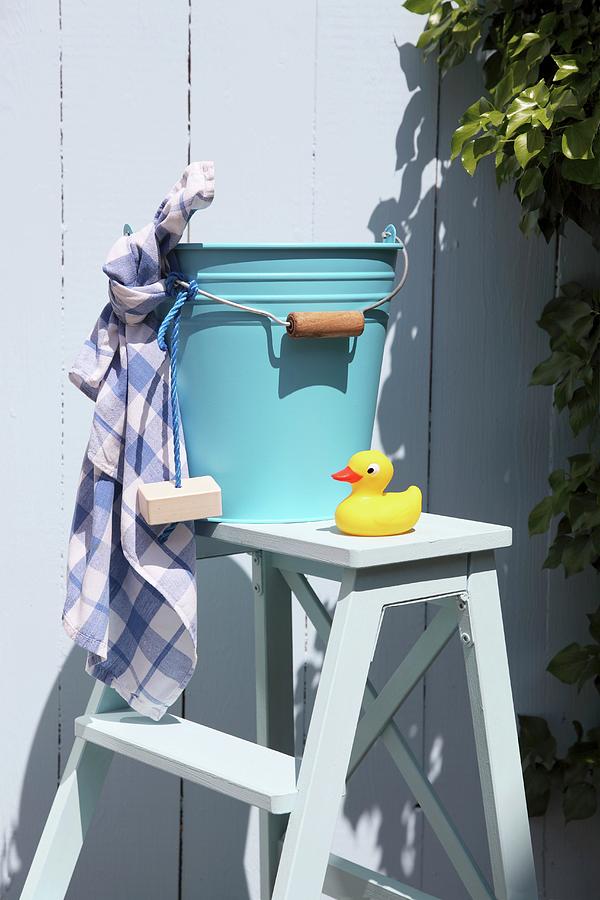 Blue Metal Bucket, Bar Of Soap, Cloth And Yellow Rubber Duck On White Wooden Step Ladder Photograph by Thordis Rggeberg