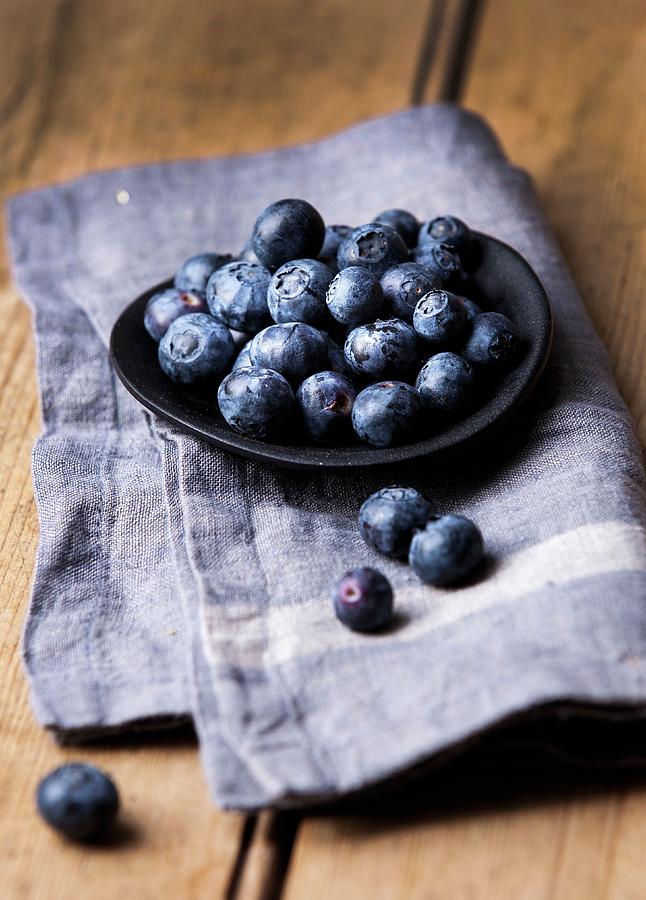 Blueberries In A Shallow Black Bowl On A Blue Linen Cloth Photograph by Stacy Grant