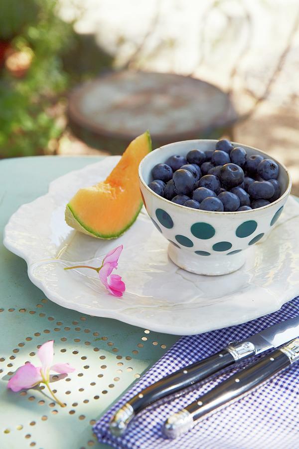 Blueberries In A Spotted Bowl And A Wedge Of Honeydew Melon With Antique Cutlery On A Bistro Table In A Garden Photograph by Jalag / Olaf Szczepaniak