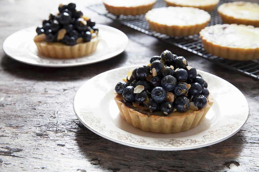 Blueberry And Vanilla Tartlets On Plates And A Cooling Rack Photograph by Andr Ainsworth