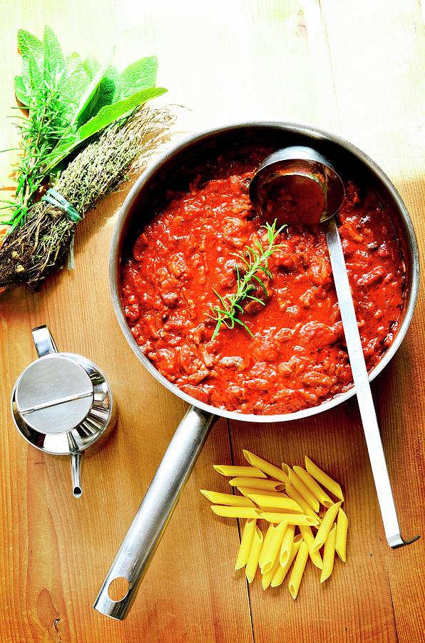 Bolognese Sauce In A Pan On A Wooden Board With Penne Pasta, Herbs And Olive Oil Photograph by Jamie Watson