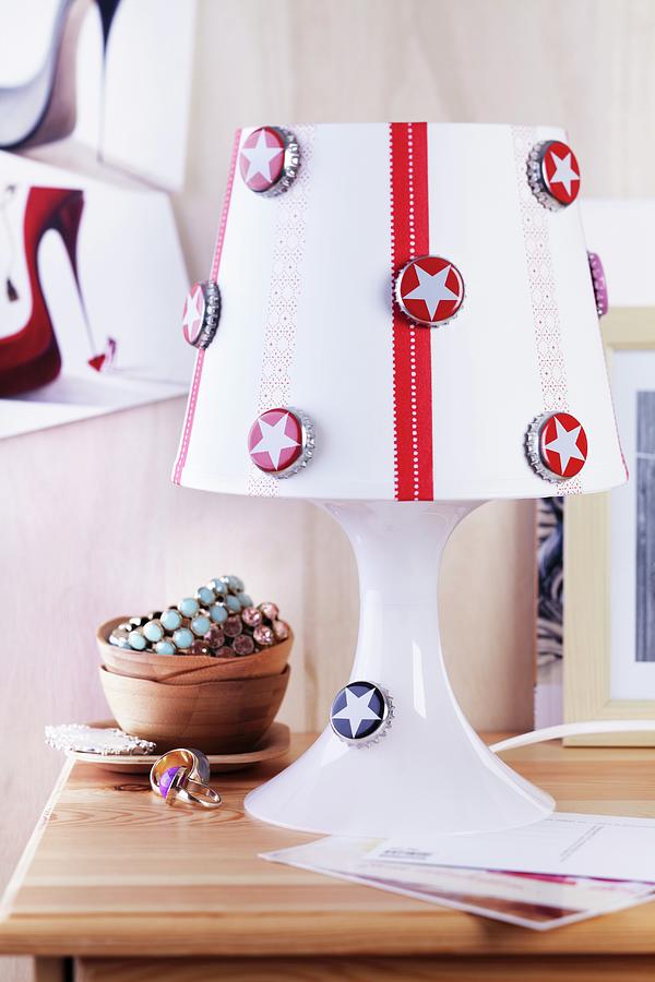 Bottle Caps Printed With Stars And Red Ribbon Decorating White Lampshade Of Table Lamp Photograph by Franziska Taube
