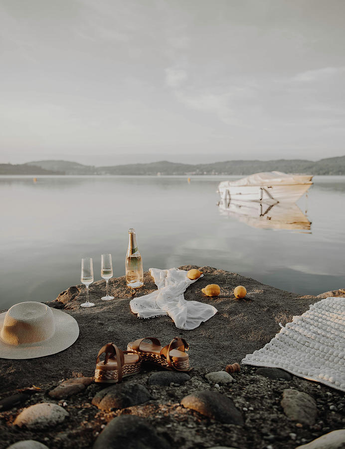Bottle Of Sparkling Wine, Glasses, Sunhat, Sandals And Blanket On Rocky Lake Shore Photograph by Agata Dimmich