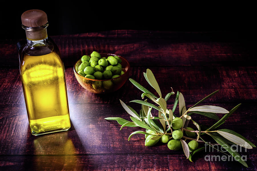 Bottle with virgin olive oil next to a bouquet of raw olives on dark background. Photograph by Joaquin Corbalan
