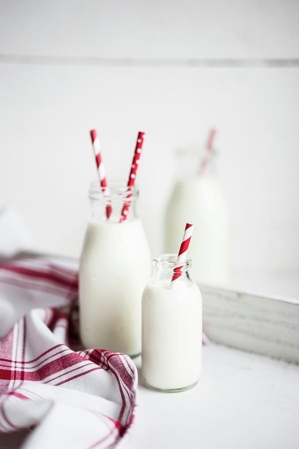 Bottles Of Milk With Red-and-white Striped Straws On A White Wooden Surface Photograph by Alena Haurylik