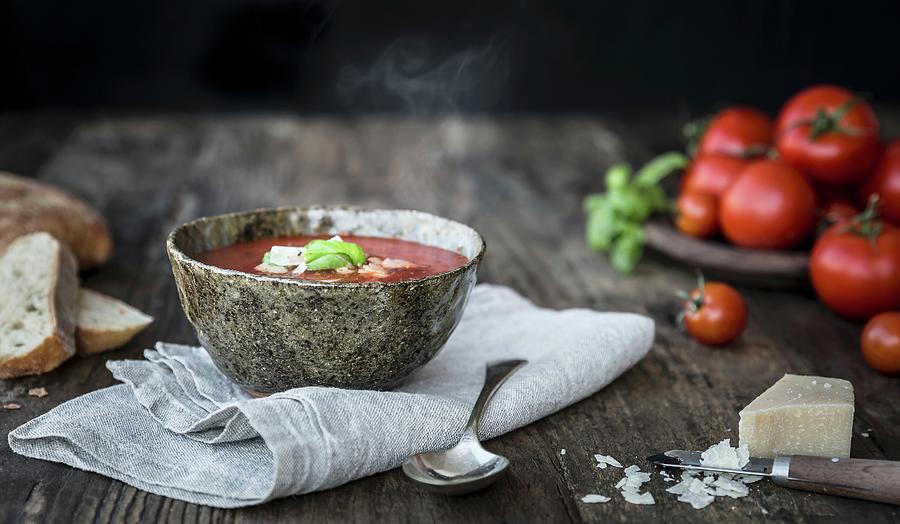Bowl Of Steaming Tomato Soup With Fresh Tomatoes Parmesan Cheese Bread And Basil On A Wooden Table Photograph by Sarah Coghill